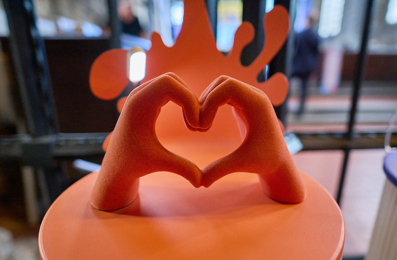 A sculpture of two orange hands forming a heart shape, displayed indoors with a blurred background, was showcased at Clerkenwell Design Week.