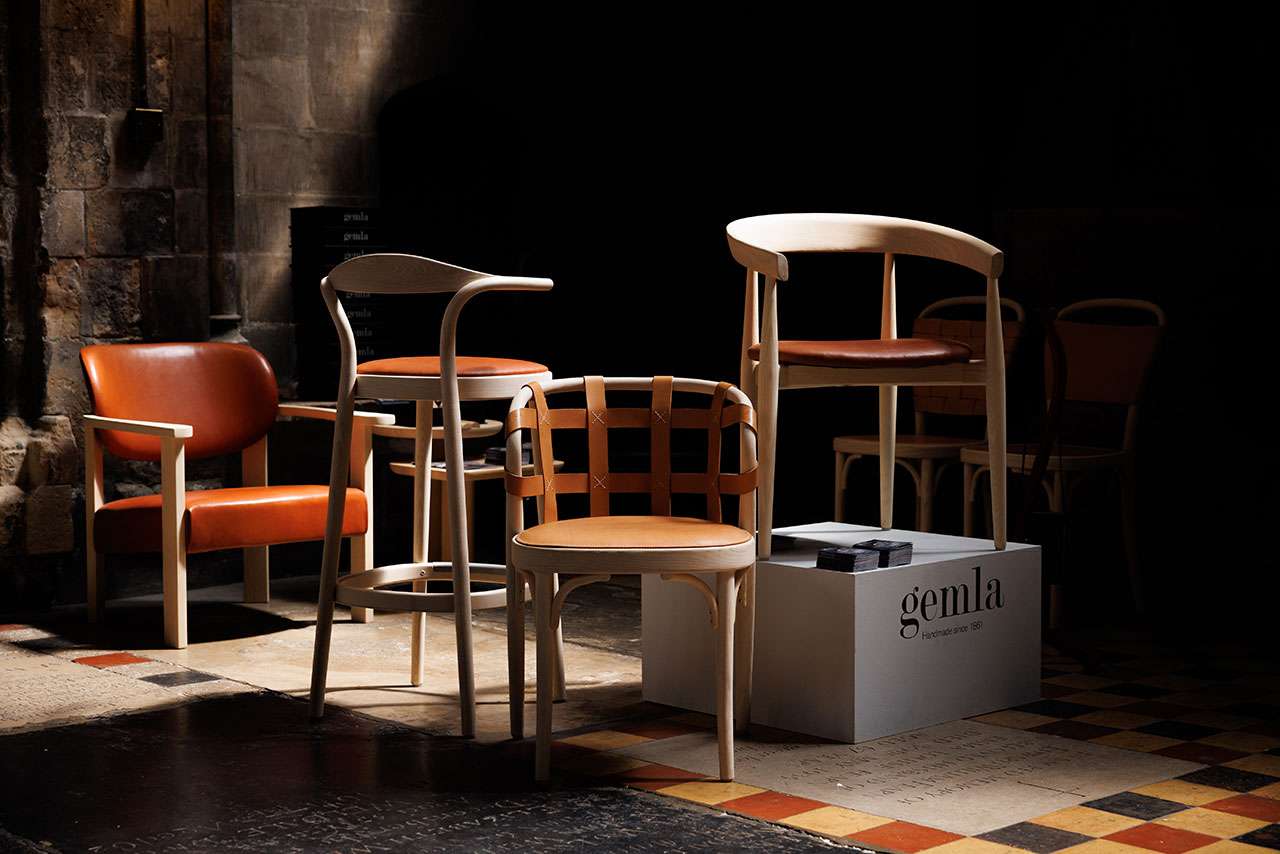 A group of modern wooden chairs with leather seats in various designs is arranged on a patterned tile floor near a display box labeled