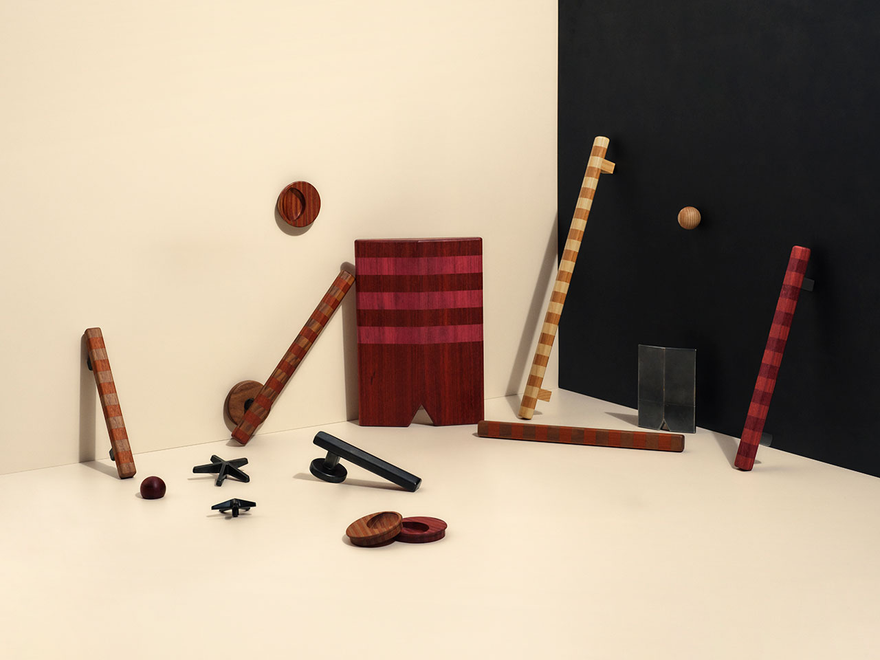 Assorted geometric wooden objects and shapes are arranged against a beige and black background, with some pieces leaning or lying flat on the surface.