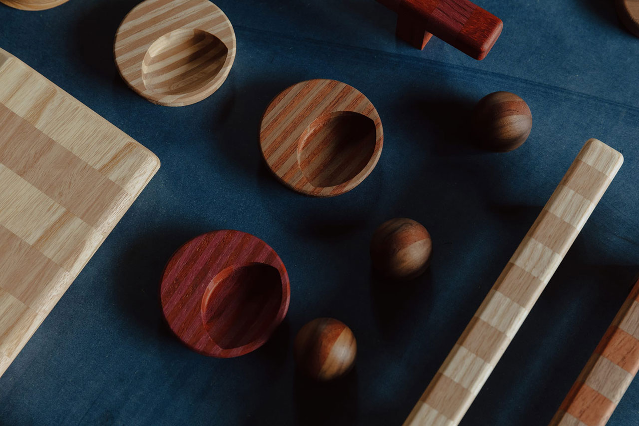 Geometric wooden objects, including round dishes, spheres, and rectangular boards, arranged on a dark blue surface.