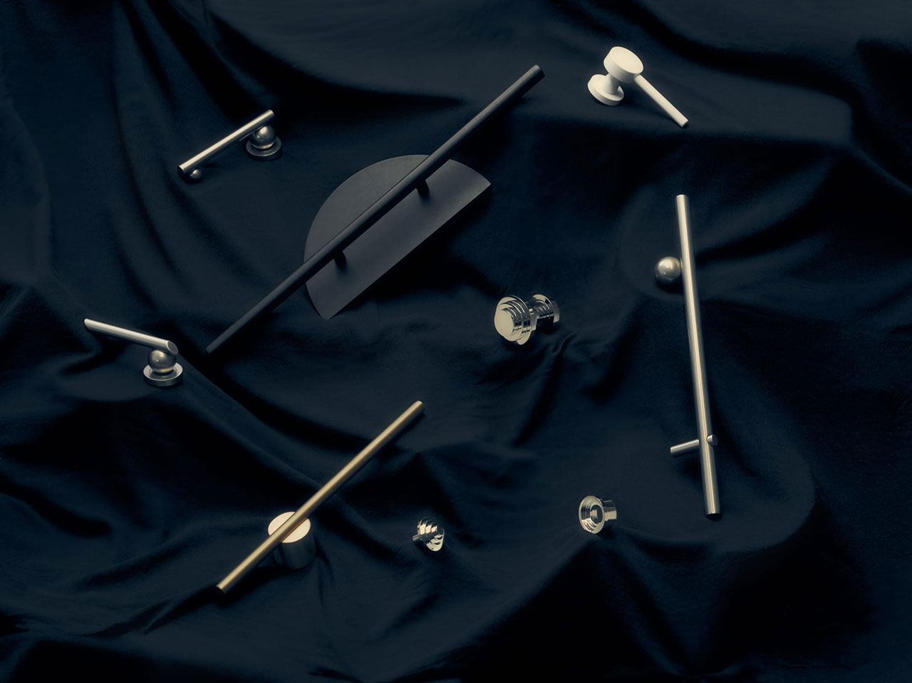 Various metal handles and knobs are arranged on a dark, draped fabric background in a flat lay composition.
