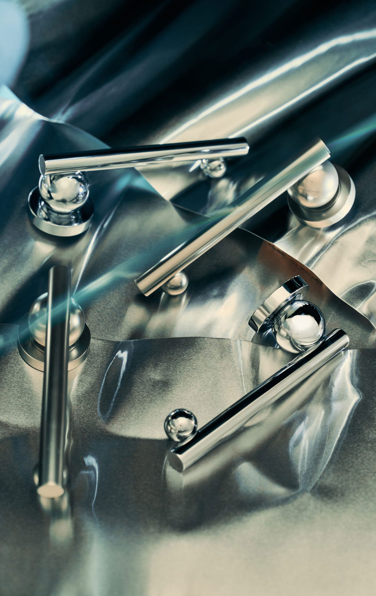 Several metallic rods and spheres are arranged on a crumpled reflective metallic surface, creating a modern, abstract composition.