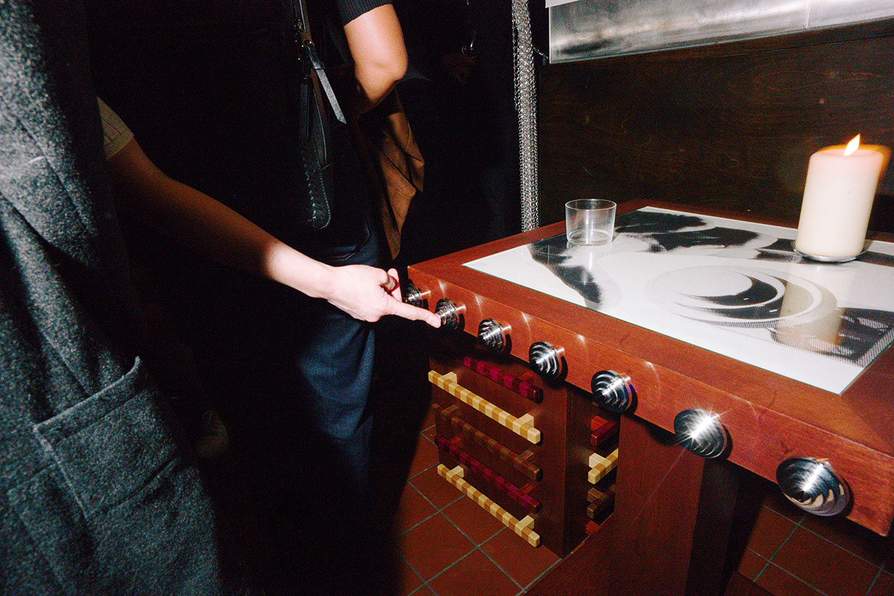 A person adjusts a knob on a Bankston foosball table; a glass and a lit candle sit on the table’s corner.