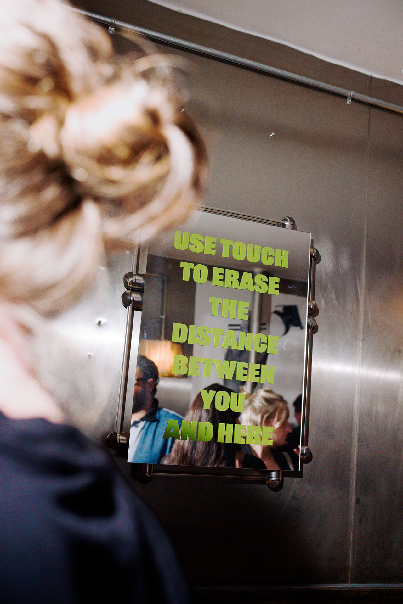 A person with blonde hair faces a mirror with green text, 