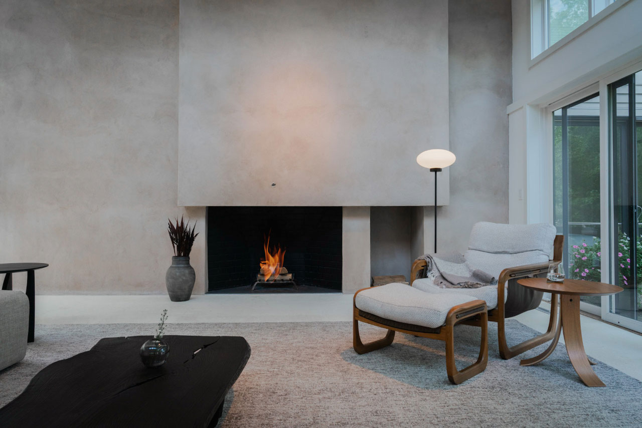 Modern living room with minimalist decor, featuring a lit fireplace, a cushioned armchair with matching ottoman, side table, and large windows letting in natural light—perfect for relaxing during your Friday Five.