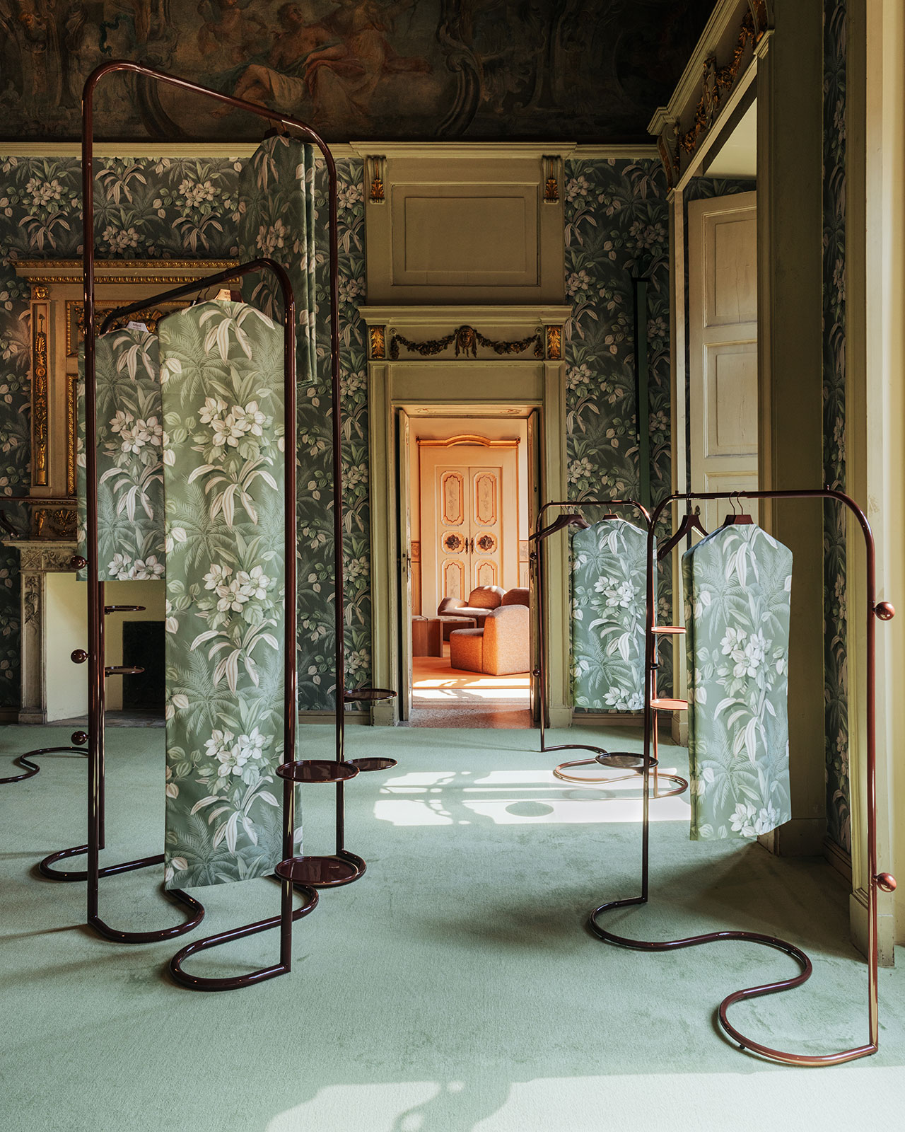 A room with green floral wallpaper and carpet, ornate molding, and several freestanding floral-patterned privacy screens arranged throughout the space.