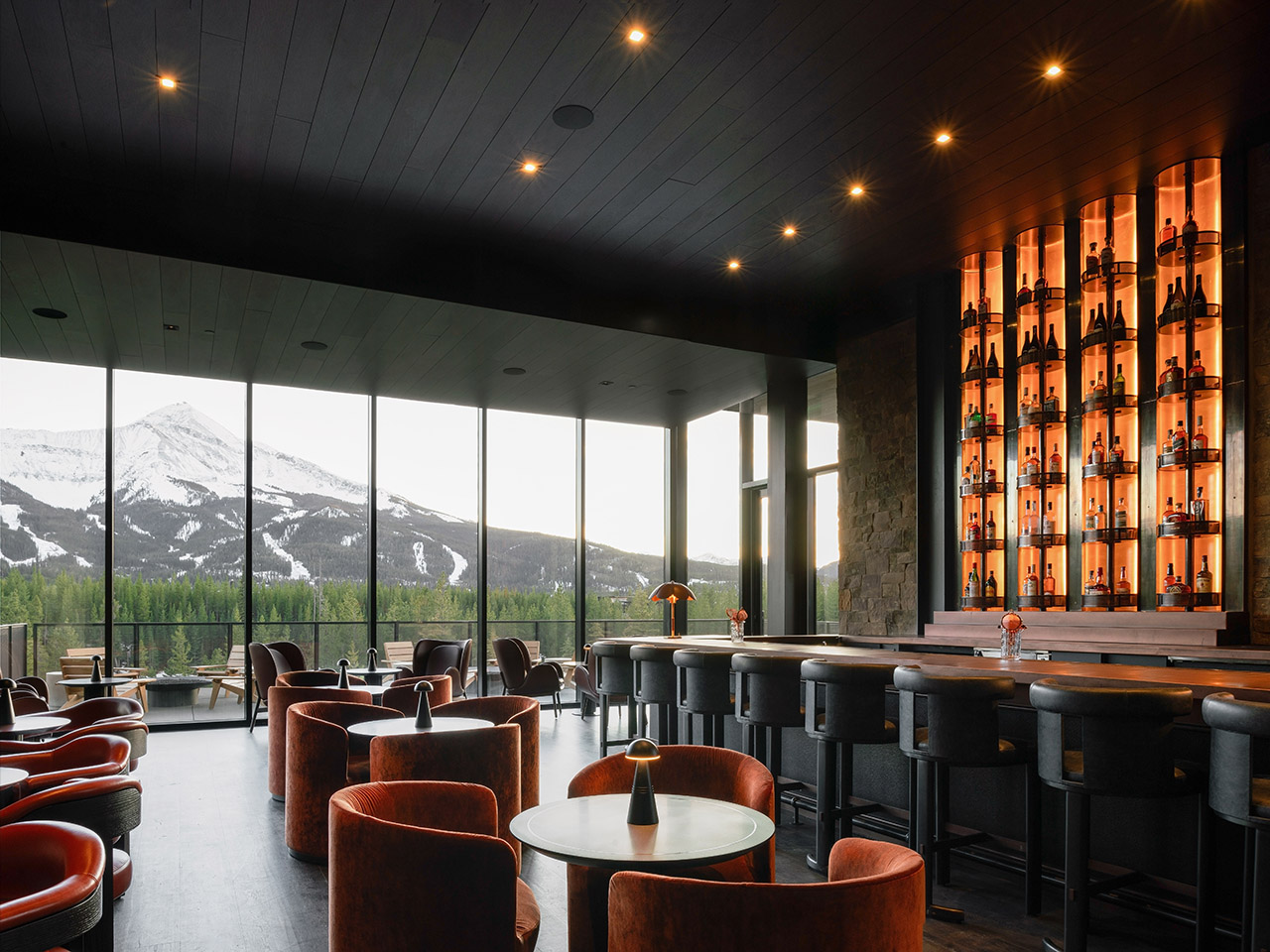 Modern lounge with a bar, seating, and large windows overlooking snow-capped mountains.