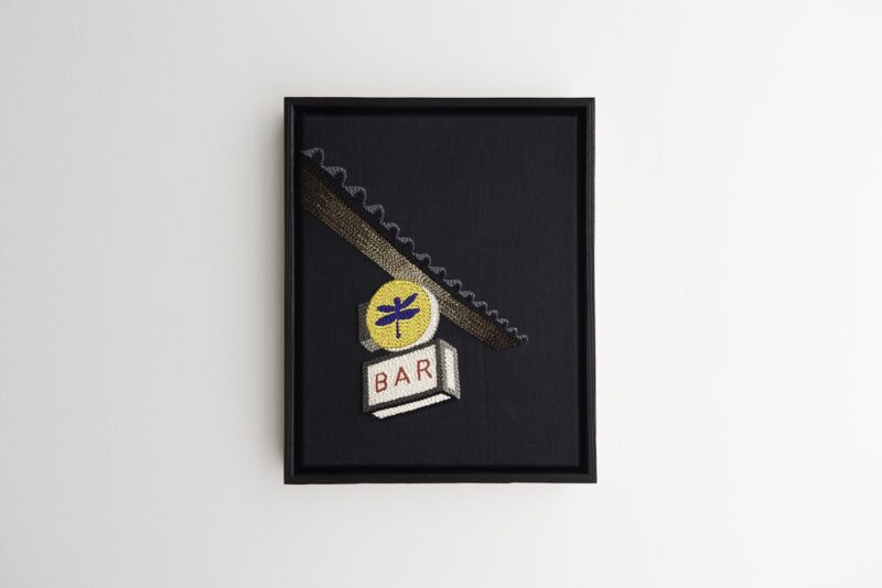 Framed embroidery of a bar sign with a dragonfly emblem and the word 