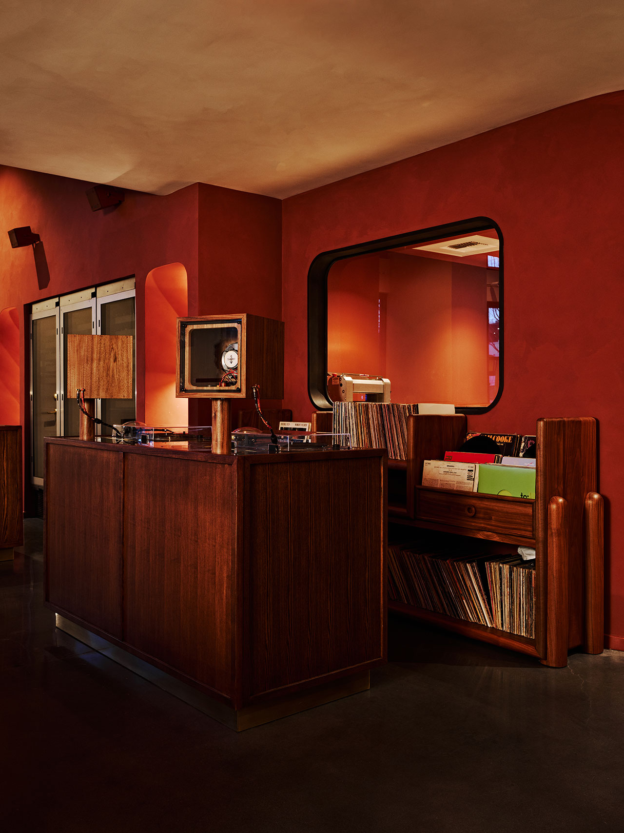 A retro-style room with a wooden counter, turntables, vinyl records, and a large mirror on a reddish-brown wall.
