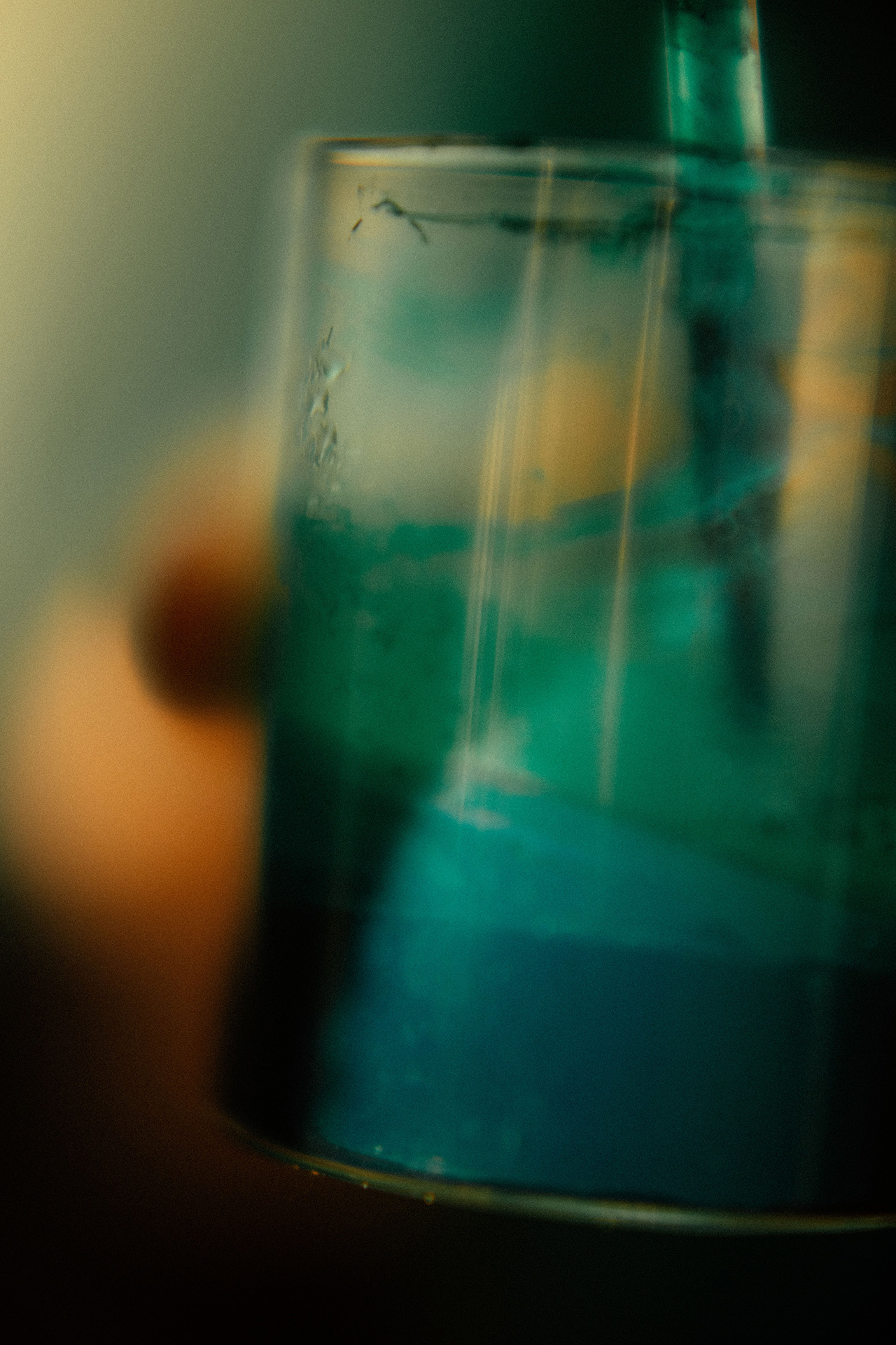 A close-up of a transparent glass with a blue-green liquid inside, featuring a straw and an out-of-focus background, evokes the clean, minimalist aesthetic often seen in Aesop campaigns.