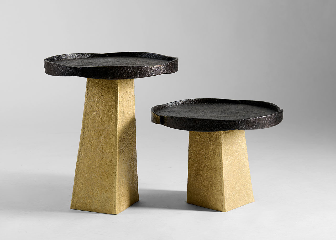 Two modern side tables with textured black round tops and tapered gold bases, displayed against a plain gray background.