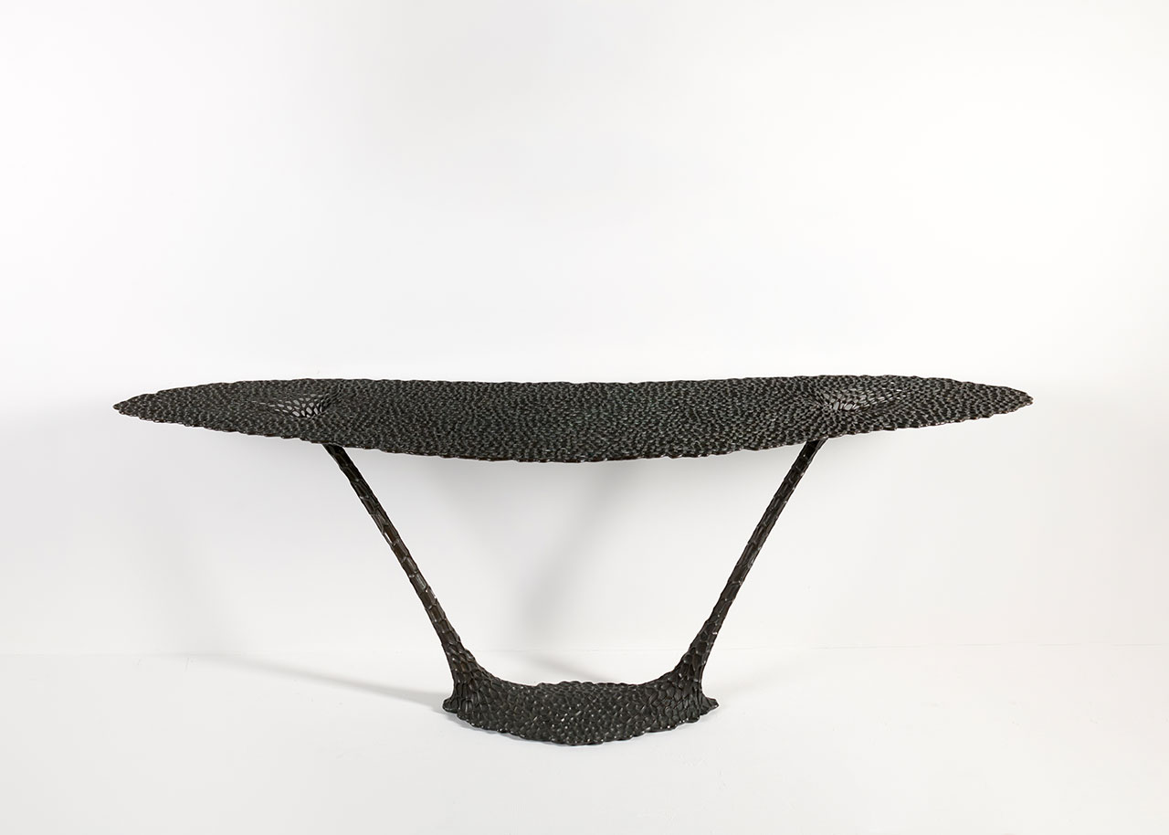 A sculptural black console table with a textured, organic surface and two angled supports connecting an oval top to an oval base, set against a plain white background.