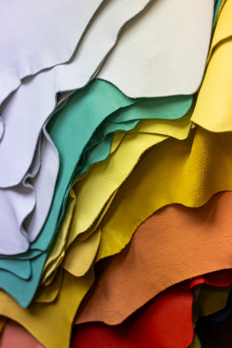 Stack of leather sheets in various colors, including white, teal, yellow, orange, and red, arranged in overlapping layers.