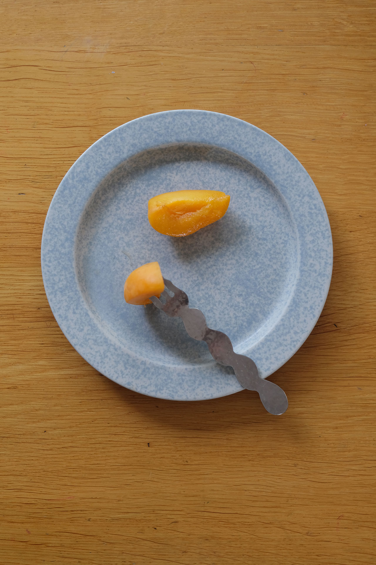 A blue speckled plate with a metal utensil holding a small orange fruit segment, and another orange fruit segment on the plate—each piece a vibrant building block of color and flavor.