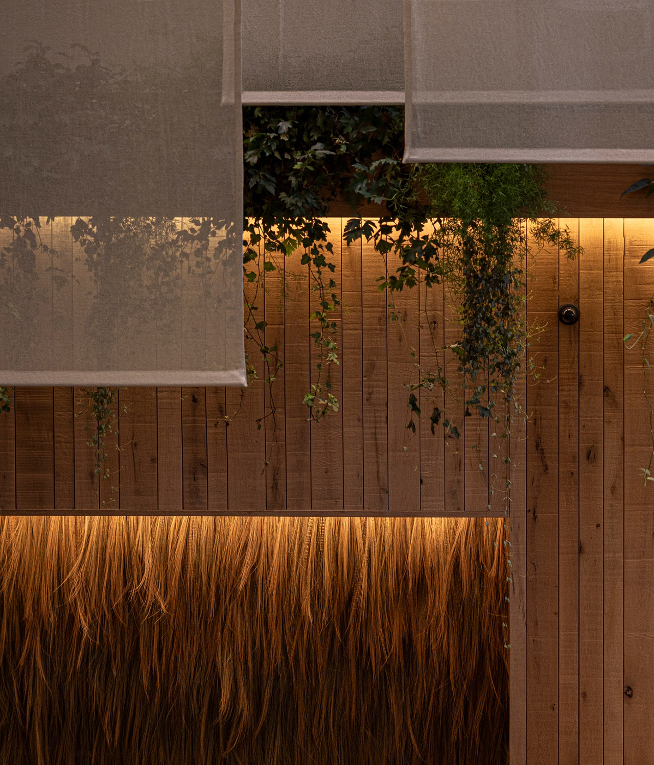Wooden wall with warm lighting, hanging greenery, and semi-transparent mesh panels suspended above, inspired by the minimalist style of Norm Architects.