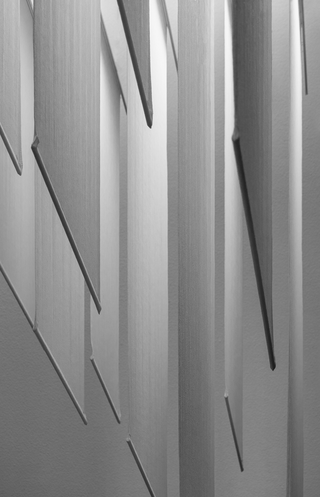 Vertical rectangular panels, inspired by Norm Architects, are arranged in parallel rows and suspended from above, casting shadows on a plain wall in a grayscale composition.