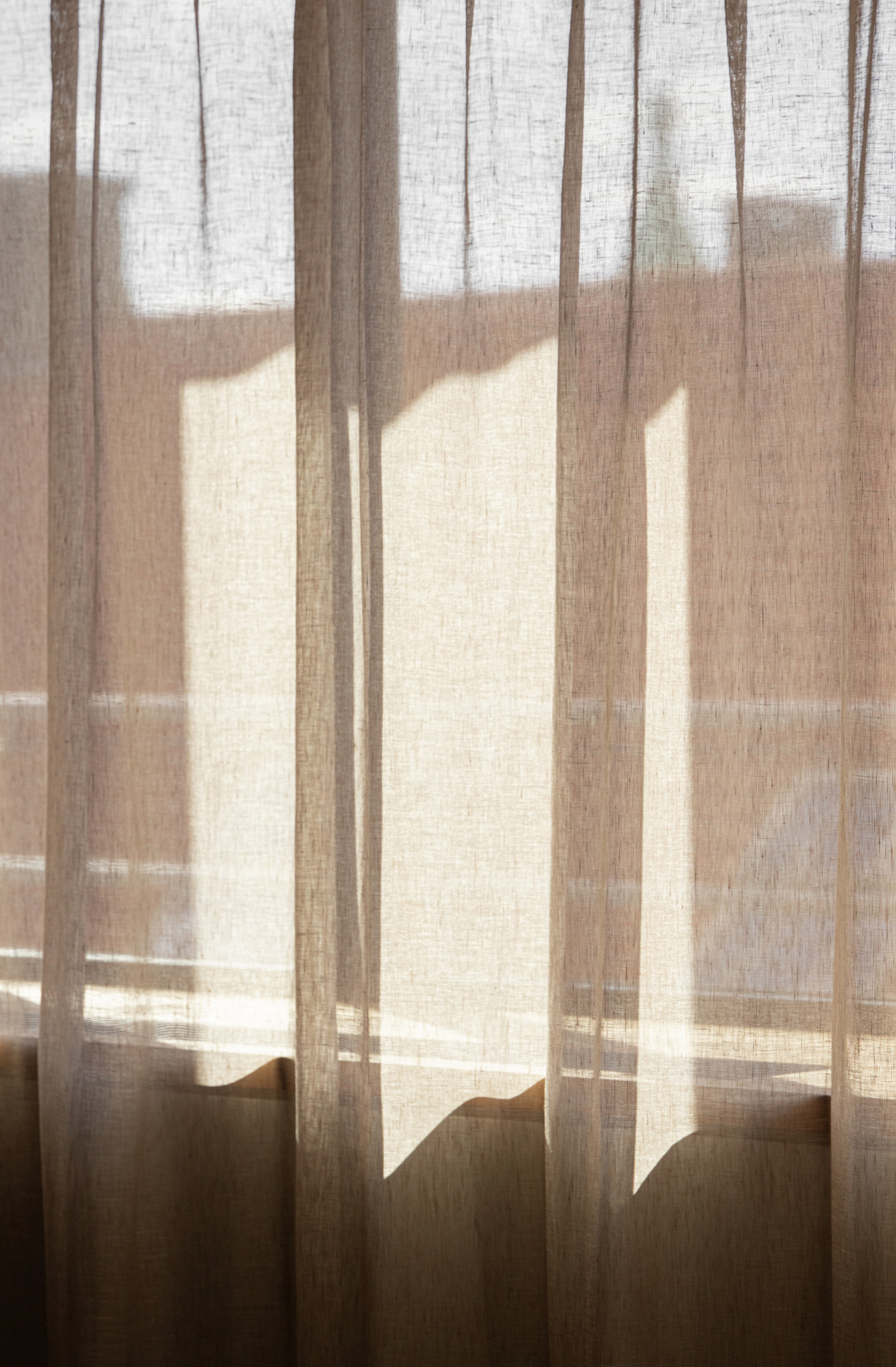 Sheer curtains hang in front of a sunlit window, casting soft shadows and letting filtered sunlight into the room, evoking the minimalist elegance favored by Norm Architects.