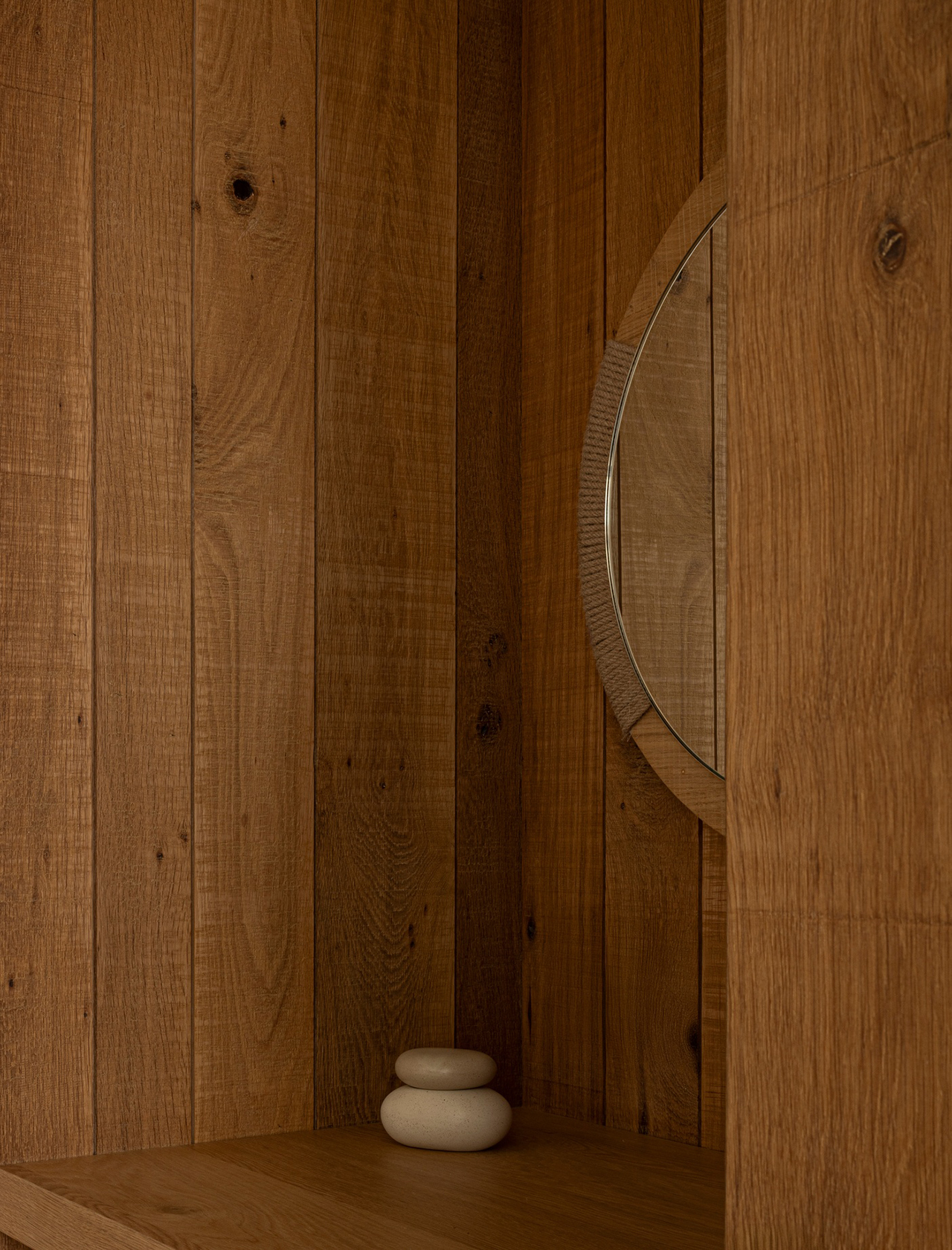 A round mirror by Norm Architects is partially visible on a wooden wall, with two stacked smooth stones placed on a wooden surface below.
