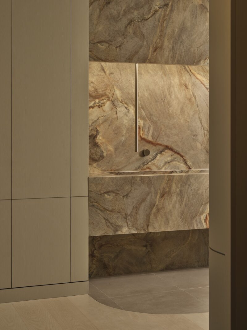 Minimalist bathroom with beige cabinetry and a walk-in shower featuring large, earth-toned marble walls and a modern, linear showerhead.