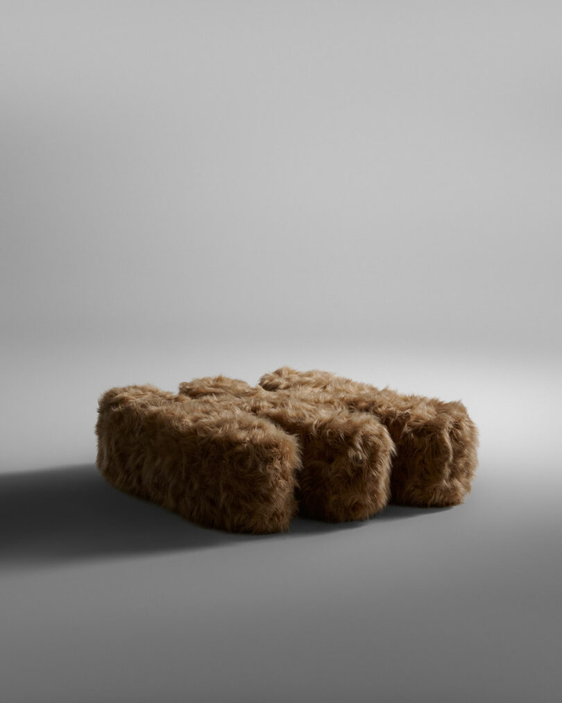 Three rectangular ottomans with brown, shaggy, fur-like upholstery are arranged side by side on a plain gray background.