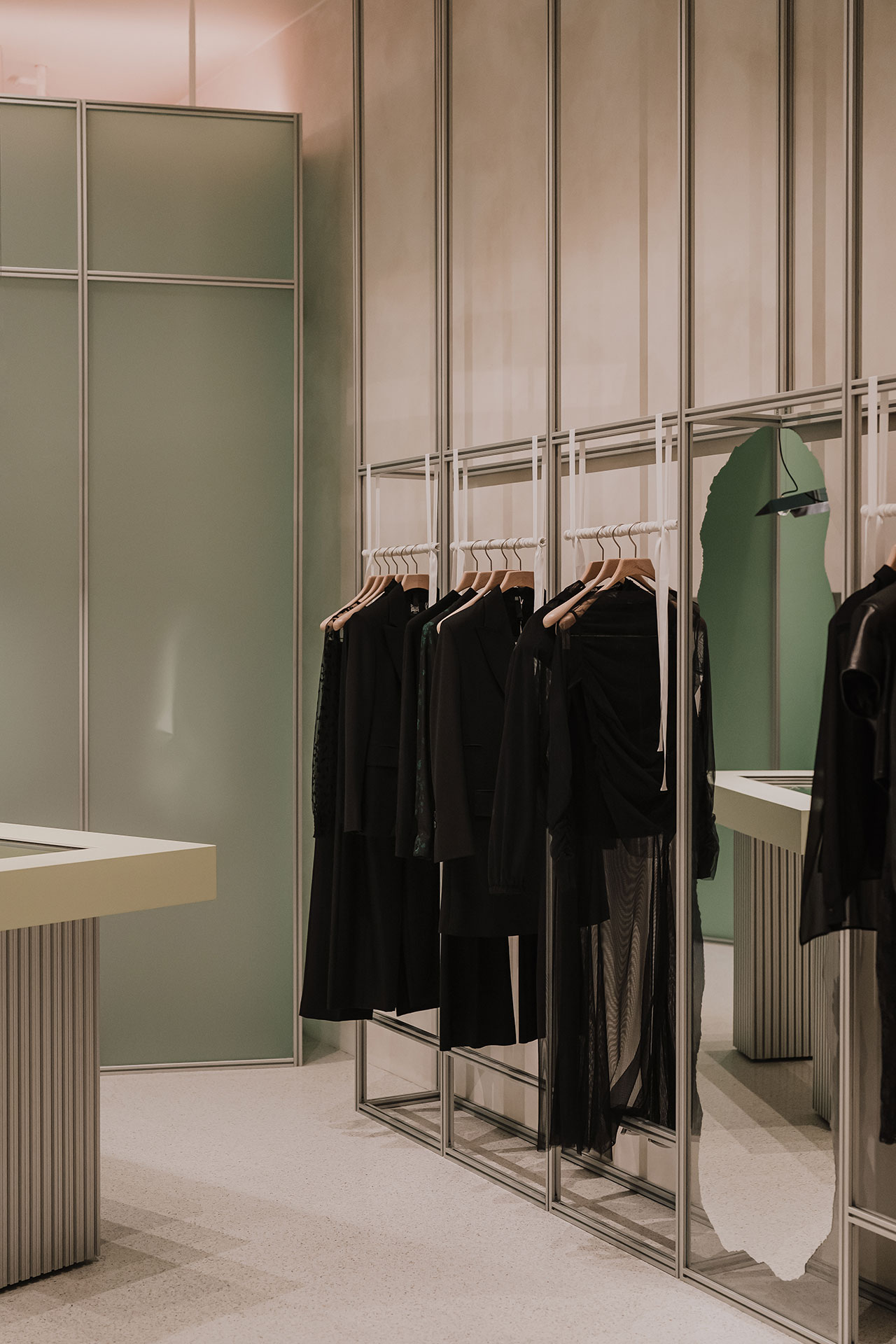Clothing store interior with several black garments hanging on wooden hangers in front of floor-to-ceiling mirrors and frosted glass partitions.