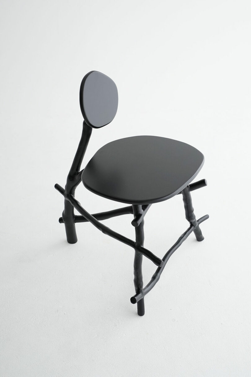 A modern black chair with a round backrest, an irregularly shaped seat, and legs and supports resembling tree branches, set against a plain white background.