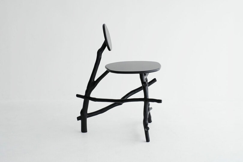A minimalist chair with a round black seat and backrest, supported by irregular, branch-like black legs and frame, set against a plain white background.