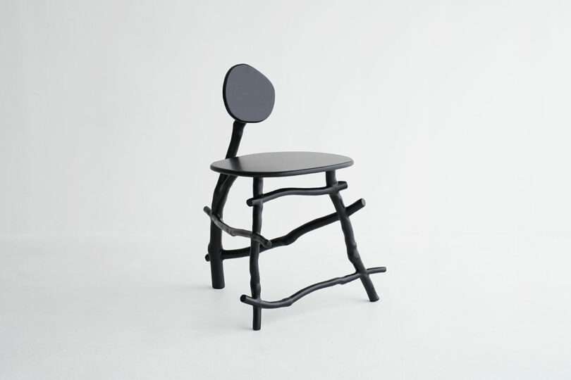 A modern black chair with a round seat, irregular stick-like legs, and an asymmetrical round backrest, set against a plain white background.