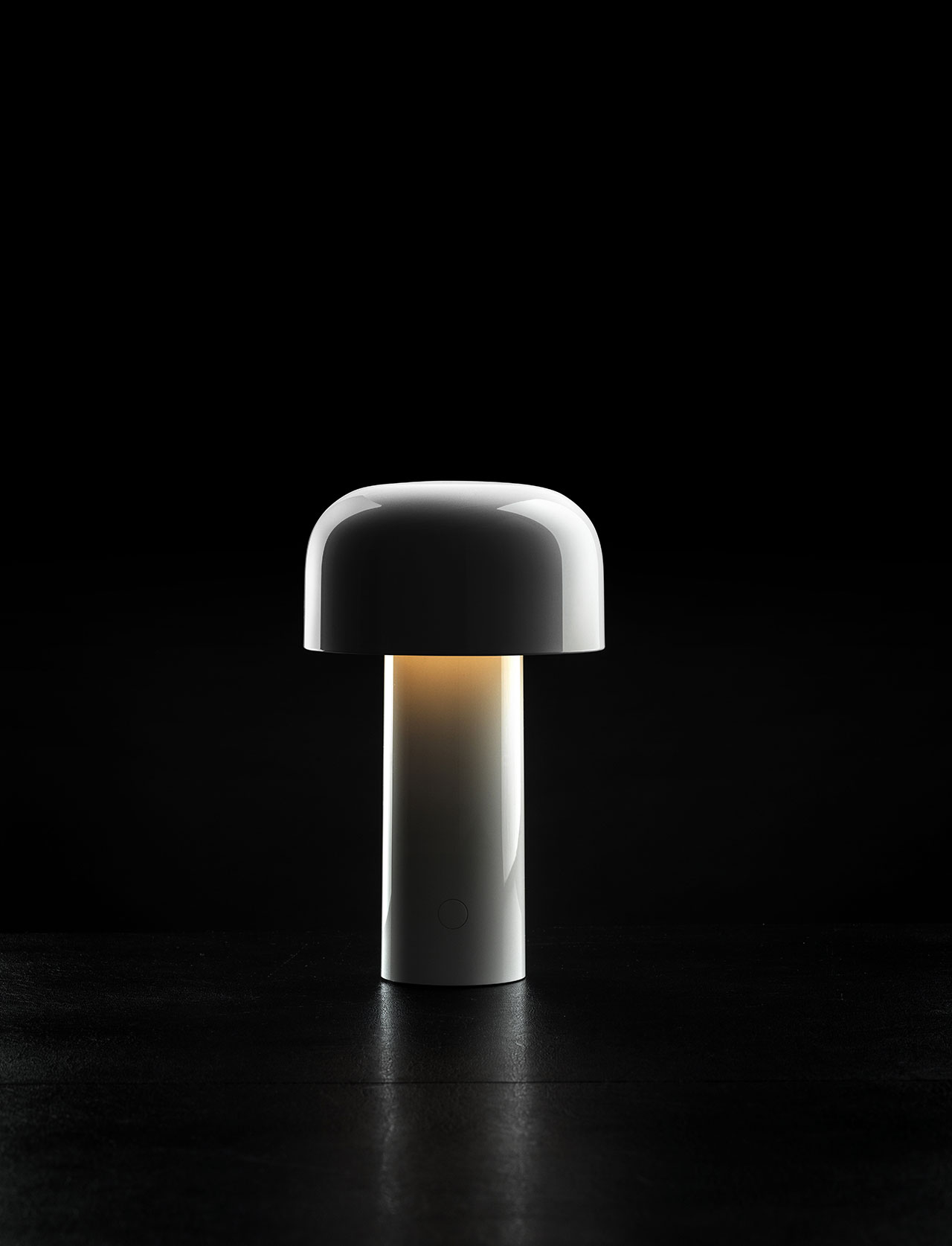 A modern, white, mushroom-shaped table lamp emits a soft light, set against a black background—bringing the cozy comfort of an Avocado mattress to your bedside.