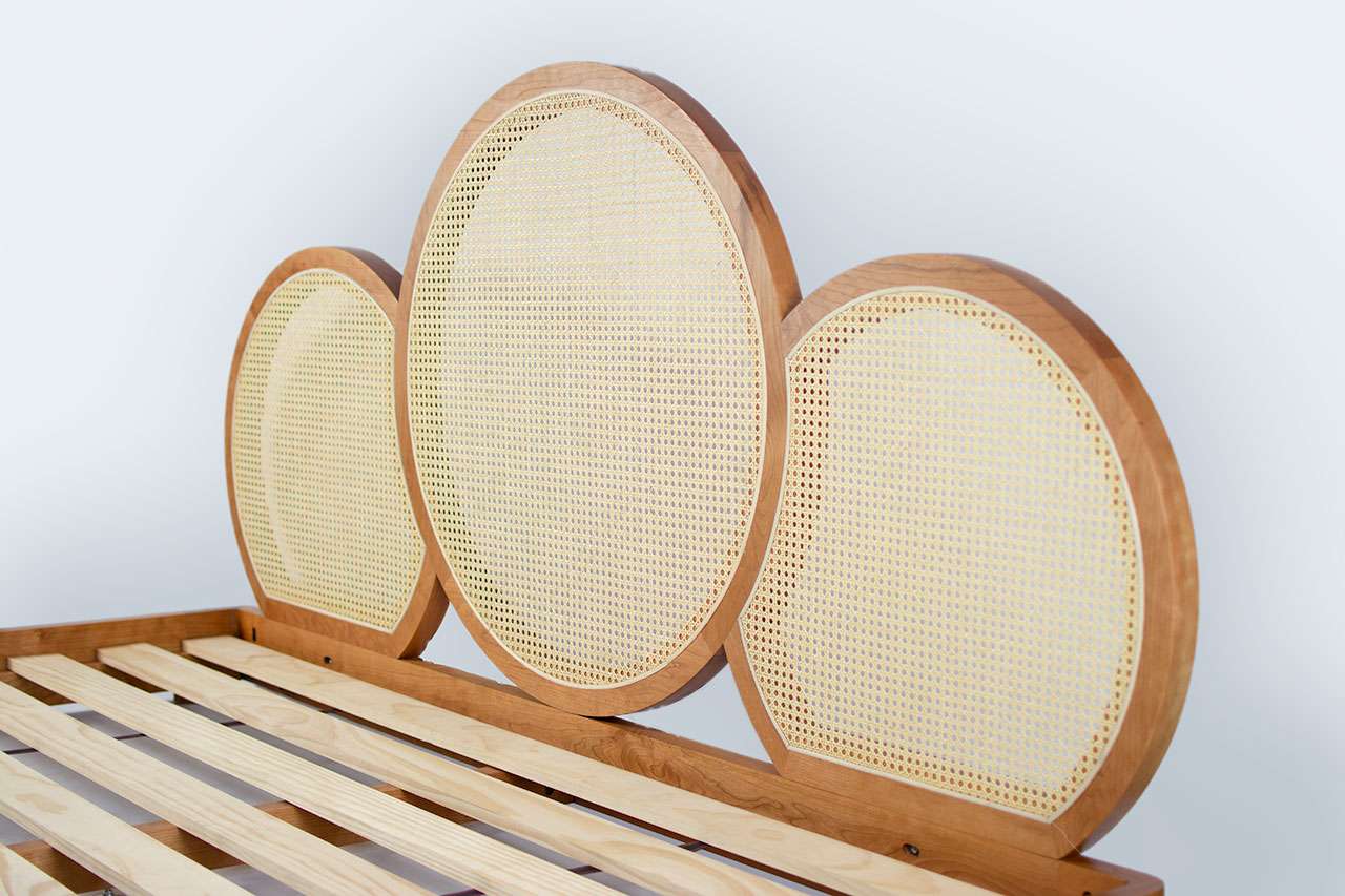 A wooden bed frame with three round, woven cane headboard panels in different sizes, arranged in a row, is perfectly paired with an Avocado mattress, set against a plain background.