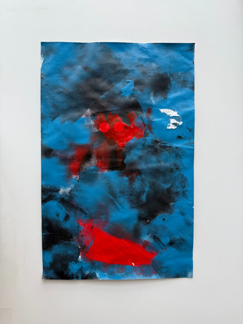 Abstract painting featuring a mix of blue, black, red, and white colors with bold red shapes and scattered cloud-like areas on a rectangular canvas against a white wall.