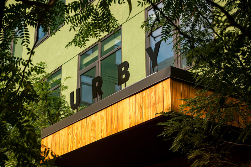 A modern building with green walls and large windows displays the black letters 
