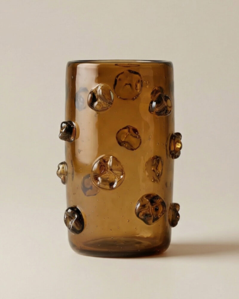 A cylindrical brown glass vase with raised, rounded decorative bumps evenly spaced on its surface, set against a light background—an elegant piece that beautifully embodies modern African decor.