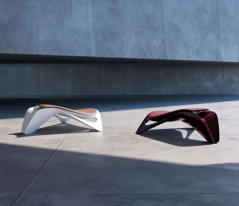 Two modern, sculptural benches—one white and one dark red, from the Ennua Element 01 collection—sit on a concrete surface against a plain gray wall, partially in shadow.
