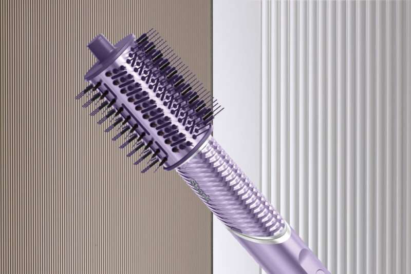 A close-up of a purple rotating hot air brush for hair styling, reminiscent of the Shark FlexStyle IonCurl, featuring bristles and a textured handle, set against a striped background.