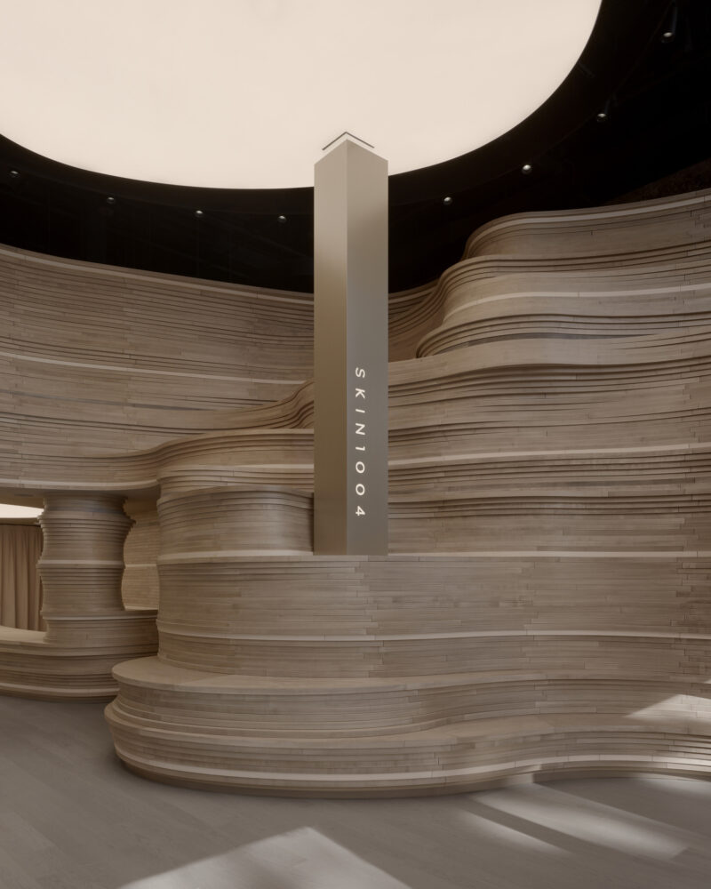 Modern interior with layered wooden walls and a tall vertical pillar displaying the word “SKIN1004” in a minimalist, softly-lit space, reflecting how SKIN1004?s first NYC store is milled from stacked wood for a warm yet contemporary ambiance.