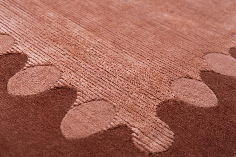 Close-up of a textured, reddish-brown Patty Studios rug featuring raised oval shapes and parallel lines in the design.