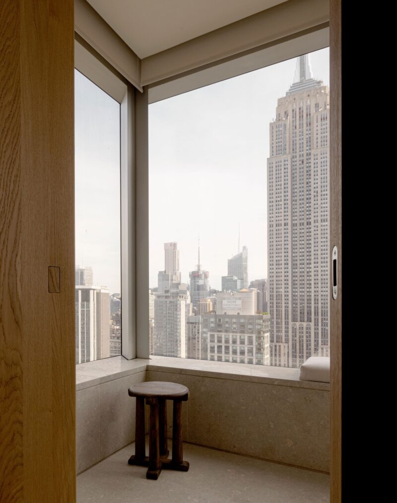 A view of the Empire State Building and Manhattan skyline from an indoor alcove with a small wooden stool.