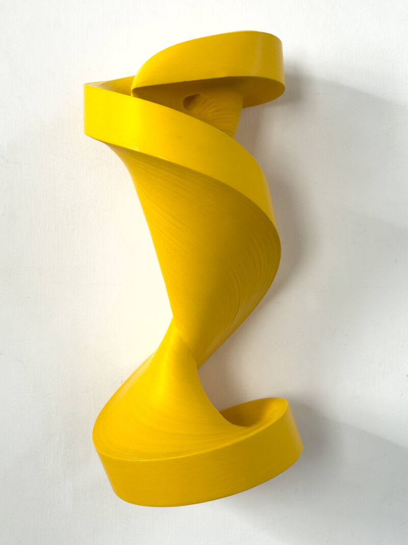 A yellow, spiral-shaped abstract wall sculpture in the style of Jae Ko.