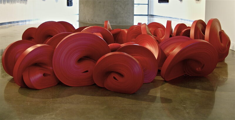 A floor installation of numerous large, bright red Jae Ko sculptures arranged in a cluster.