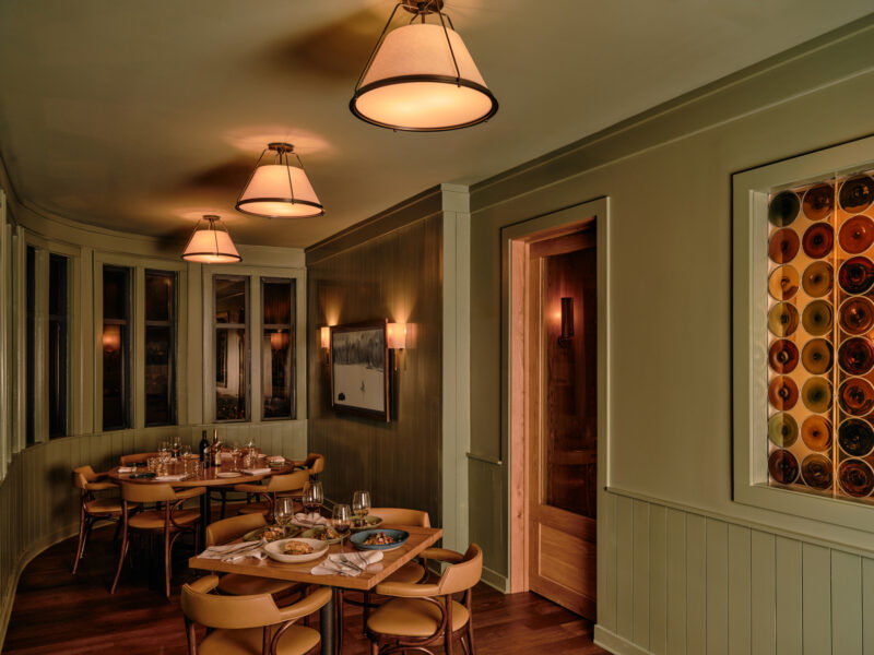 A dimly lit restaurant dining room with two tables set for dinner and a decorative wall display of circular glass panels.