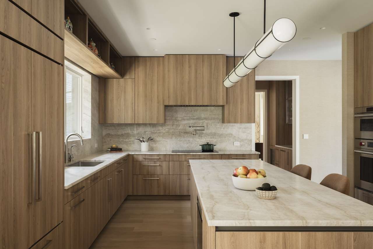 A modern kitchen with wood cabinets, stone countertops, a large island, and a cylindrical pendant light.
